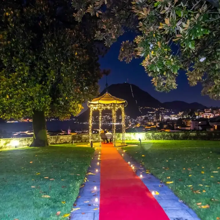 Red carpet illuminato verso un gazebo in giardino, allestimento serale di un evento
